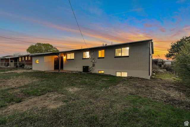 back of house at dusk with a patio area, fence, brick siding, a lawn, and central AC
