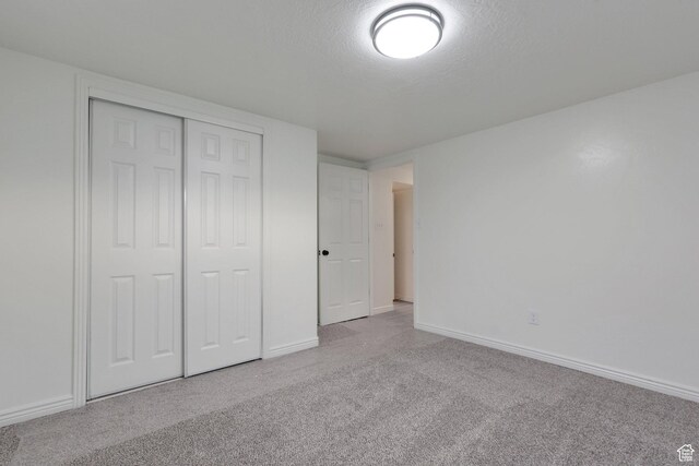 unfurnished bedroom with a closet, carpet flooring, a textured ceiling, and baseboards
