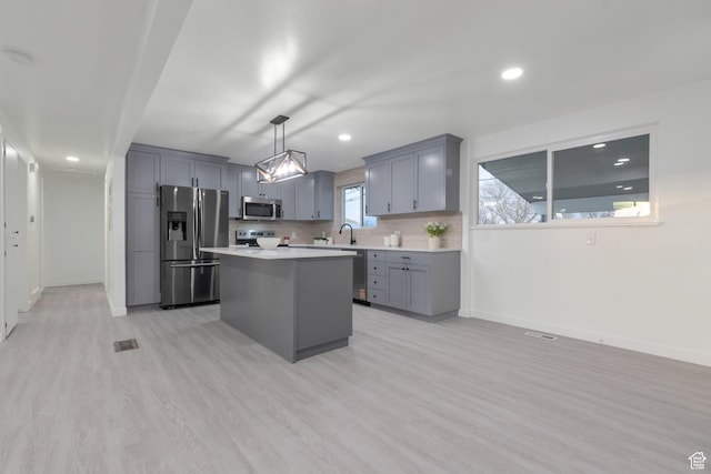 kitchen featuring light countertops, a sink, appliances with stainless steel finishes, gray cabinetry, and light wood-style floors