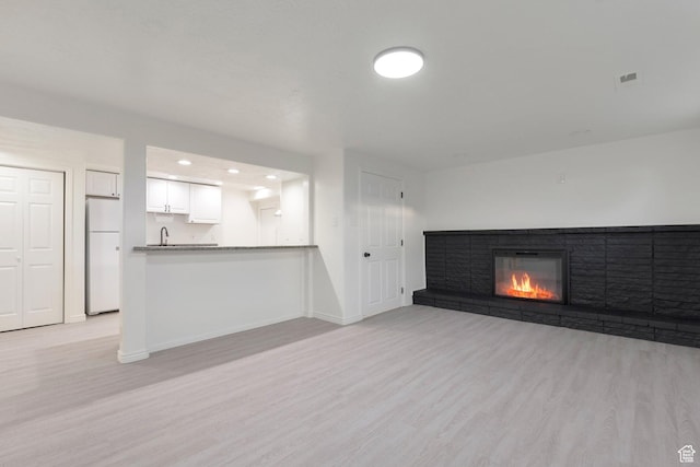 unfurnished living room with a brick fireplace, baseboards, visible vents, light wood-style floors, and recessed lighting