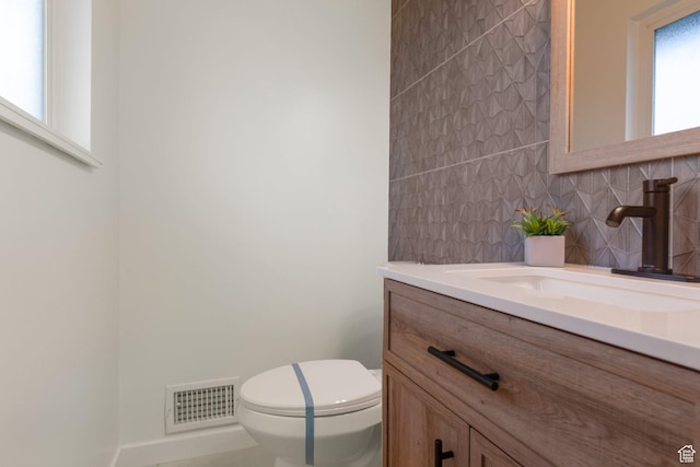 bathroom featuring decorative backsplash, visible vents, toilet, and vanity