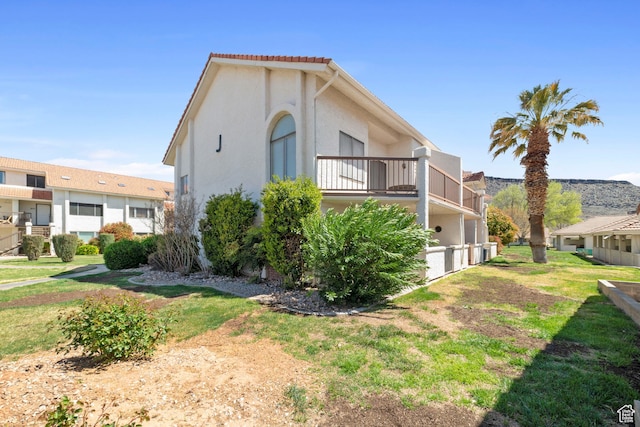 view of side of property featuring stucco siding, a lawn, and a balcony
