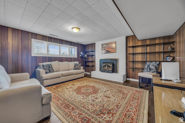 living room with a brick fireplace, wood walls, built in shelves, and wood finished floors