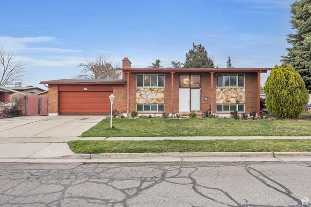 bi-level home featuring driveway, a front lawn, brick siding, a garage, and a chimney