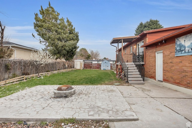 view of yard with stairs, a fenced backyard, a storage shed, and a patio area