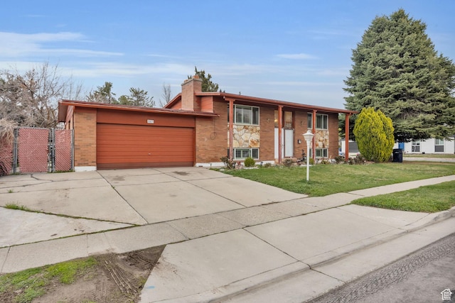 bi-level home featuring a gate, a garage, concrete driveway, a front yard, and brick siding