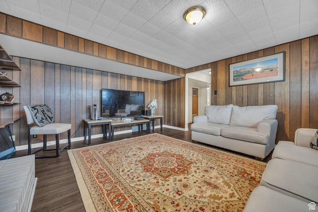 living room featuring dark wood-type flooring, baseboards, and wood walls