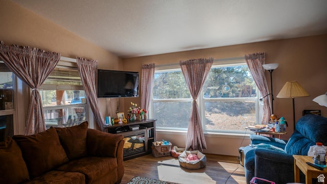 living room with a wealth of natural light, wood finished floors, and vaulted ceiling
