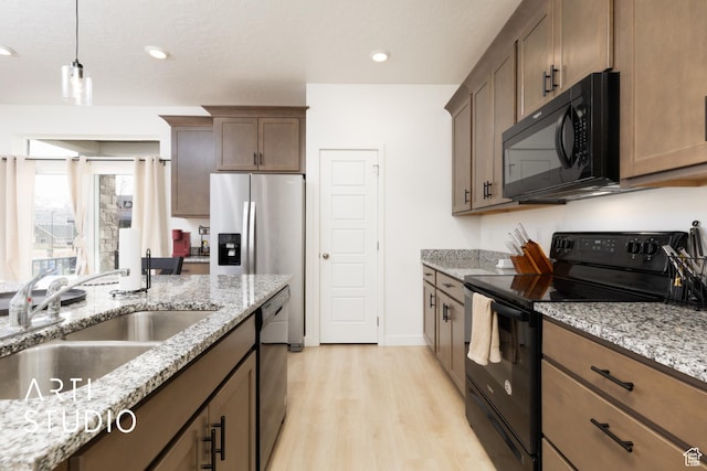 kitchen featuring decorative light fixtures, light wood-type flooring, a sink, light stone counters, and black appliances