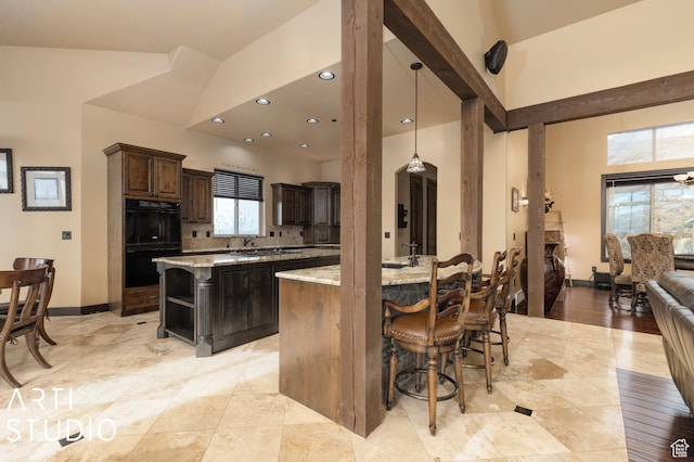 5055 Waterfall Dr, Pleasant View, UT 84414 - kitchen with dobule oven black, a towering ceiling, dark brown cabinets, light stone counters, and a center island