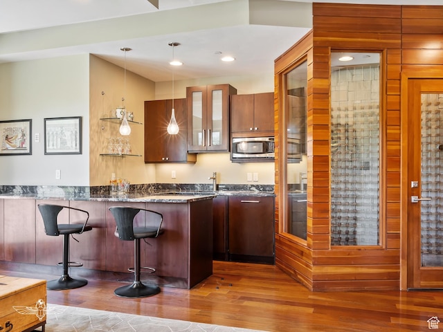 6639 E Chaparral Rd, Huntsville, UT 84317 - kitchen featuring a kitchen bar, stainless steel microwave, pendant lighting, glass insert cabinets, and wood finished floors