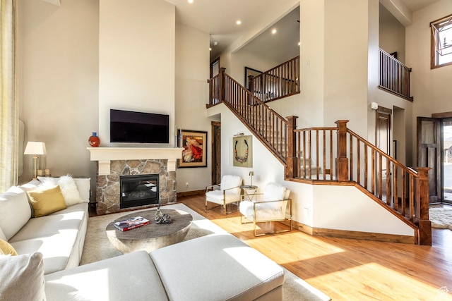living room with baseboards, stairs, wood finished floors, and a stone fireplace