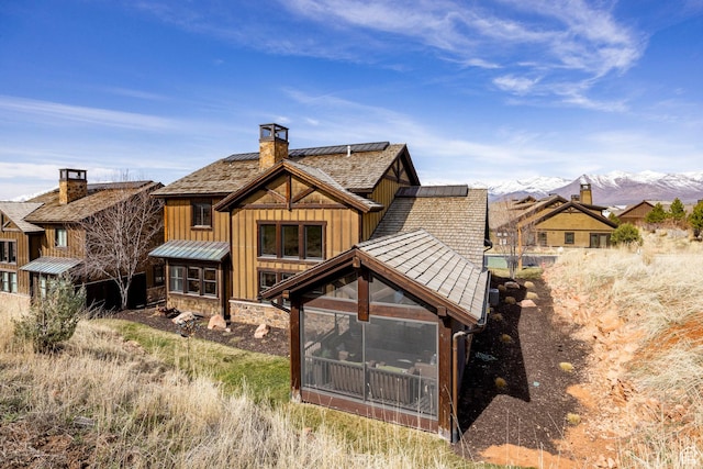 rear view of property featuring a chimney, a standing seam roof, metal roof, and roof mounted solar panels
