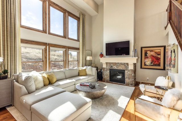 living room featuring a towering ceiling, baseboards, a fireplace, and wood finished floors