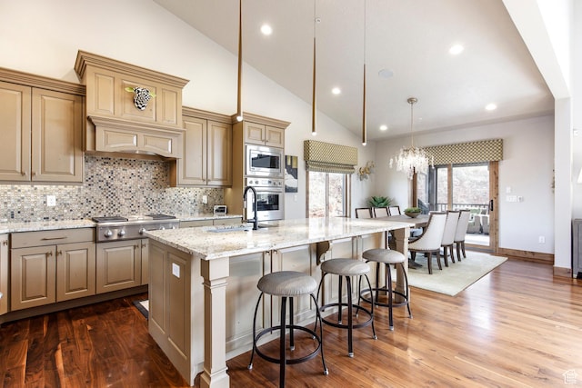 kitchen with stainless steel appliances, backsplash, a sink, an island with sink, and light stone counters