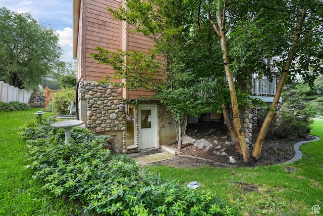 rear view of property featuring stone siding, a yard, and fence