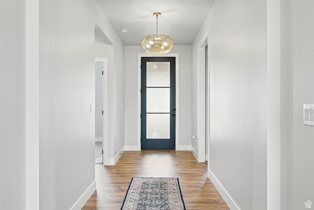 doorway featuring baseboards, a notable chandelier, and wood finished floors