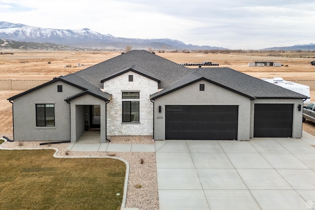 view of front facade featuring stone siding, a garage, concrete driveway, roof with shingles, and a mountain view