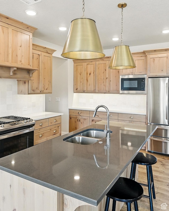 kitchen featuring light wood-style flooring, a breakfast bar, stainless steel appliances, a sink, and light brown cabinetry