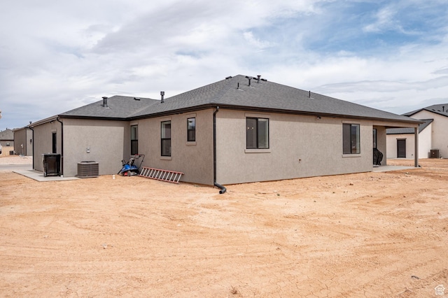 rear view of house with stucco siding, central air condition unit, a patio, and a shingled roof