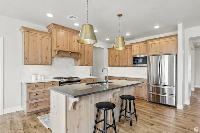 kitchen with a sink, light brown cabinetry, light wood-style flooring, and appliances with stainless steel finishes