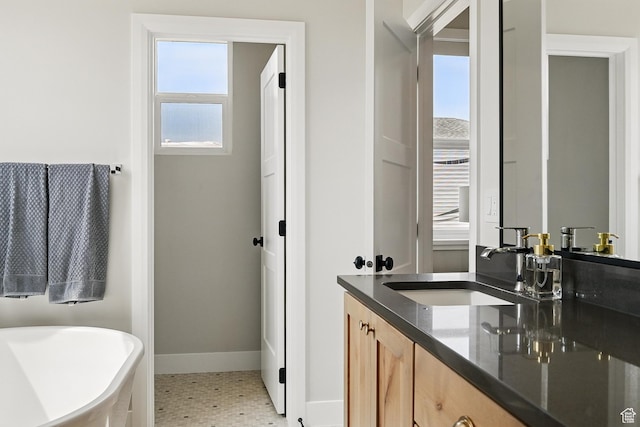 bathroom featuring a soaking tub, double vanity, a sink, and baseboards