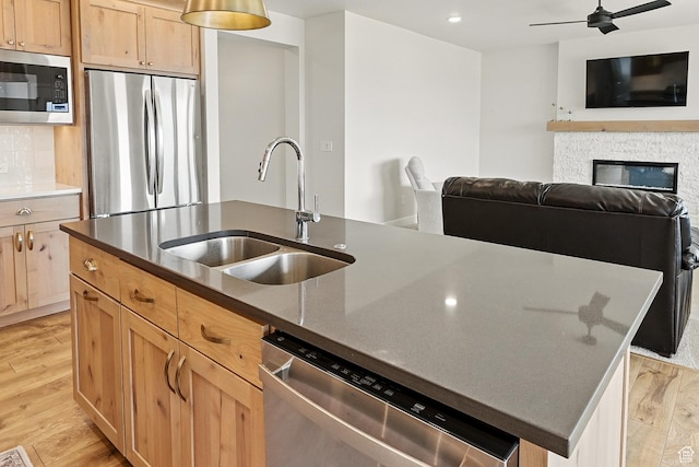 kitchen with a sink, backsplash, appliances with stainless steel finishes, light wood-type flooring, and open floor plan