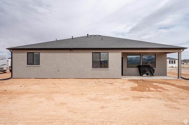 rear view of house featuring stucco siding, a shingled roof, and a patio