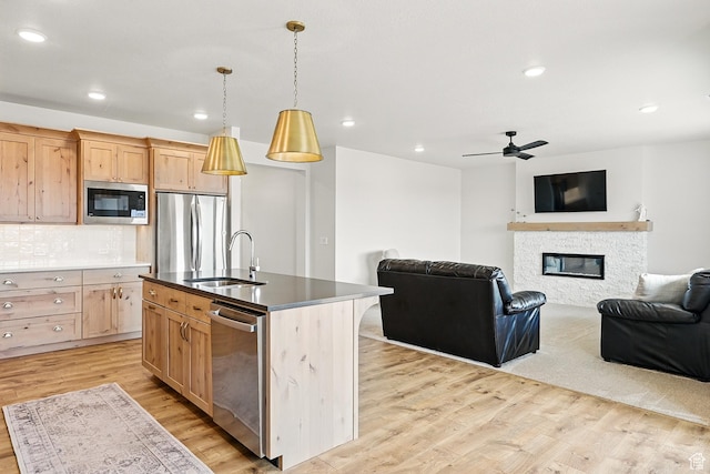 kitchen featuring a sink, light brown cabinetry, light wood-type flooring, open floor plan, and stainless steel appliances