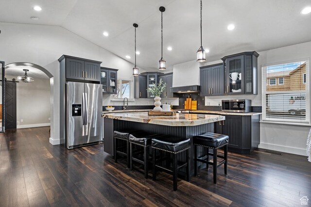 kitchen featuring custom exhaust hood, stainless steel appliances, arched walkways, glass insert cabinets, and dark wood-type flooring