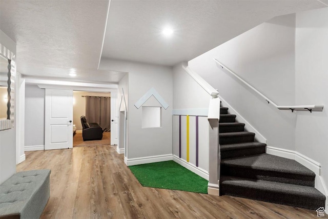 stairs featuring a textured ceiling, baseboards, and wood finished floors