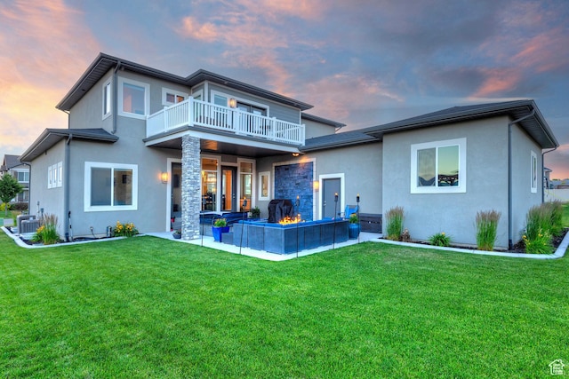 back of house at dusk featuring stucco siding, a patio, a balcony, central AC unit, and a lawn