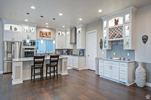 kitchen with white cabinetry, stainless steel appliances, dark wood finished floors, a kitchen island, and wall chimney range hood