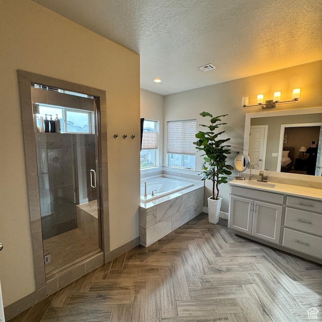 full bathroom featuring vanity, a textured ceiling, a stall shower, a garden tub, and visible vents
