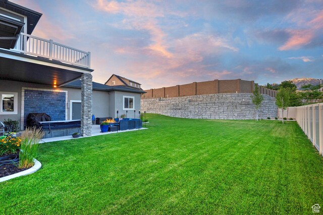 yard at dusk with a balcony, a hot tub, a fenced backyard, and a patio
