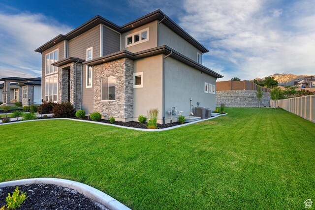 view of side of home featuring stone siding, fence, a lawn, and stucco siding