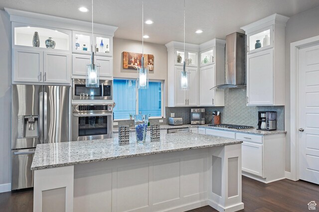kitchen with wall chimney range hood, white cabinetry, backsplash, and stainless steel appliances