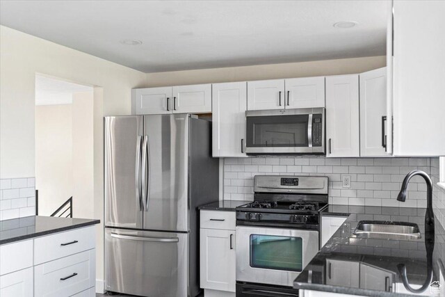 kitchen with a sink, tasteful backsplash, appliances with stainless steel finishes, white cabinets, and dark stone counters