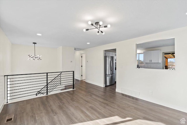 spare room featuring baseboards, a notable chandelier, visible vents, and wood finished floors