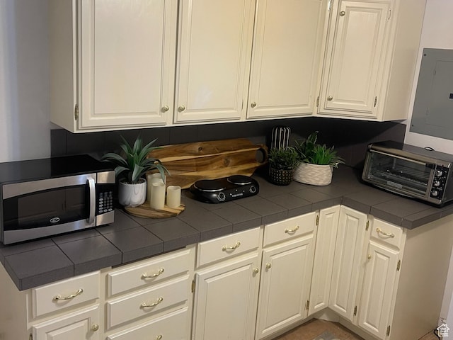 6958 S Sunrise Hills Cir E, Cottonwood Heights, UT 84121 - kitchen with stainless steel microwave, white cabinetry, electric panel, a toaster, and tile countertops