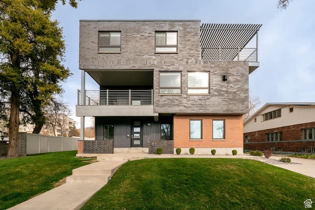 view of front of house with a balcony, brick siding, fence, and a front yard