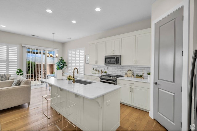 kitchen featuring white cabinetry, stainless steel appliances, decorative backsplash, a sink, and light wood-style floors