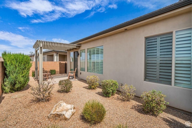 view of side of property featuring a patio, stucco siding, fence, and a pergola