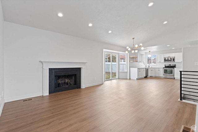 4489 W Black Elk Way, West Jordan, UT 84088 - unfurnished living room with light wood-style flooring, visible vents, a chandelier, a fireplace, and recessed lighting