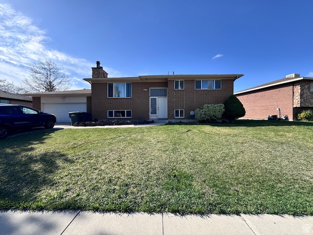split foyer home with an attached garage, a chimney, brick siding, and a front yard