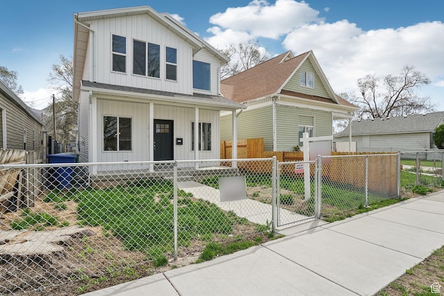 view of front of property featuring board and batten siding, a fenced front yard, covered porch, a front yard, and a gate
