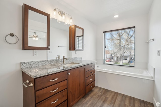 bathroom with ceiling fan, vanity, wood finished floors, and a garden tub