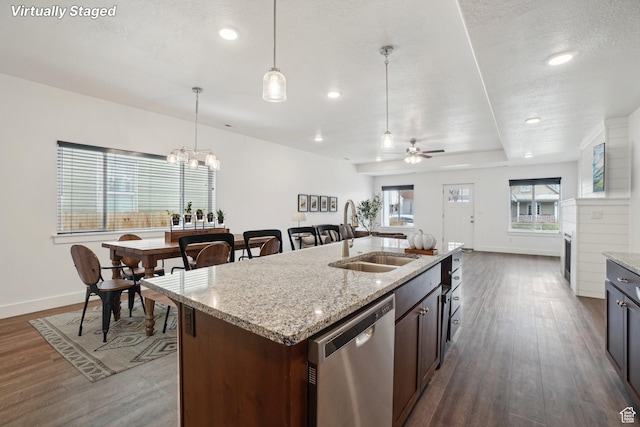 kitchen featuring dark wood-type flooring, stainless steel dishwasher, pendant lighting, ceiling fan with notable chandelier, and a sink