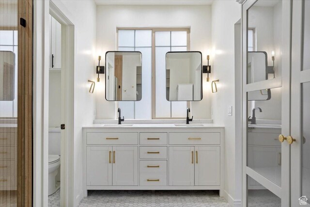 full bathroom with double vanity, a sink, and toilet