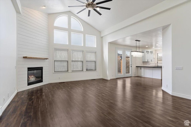 unfurnished living room with a large fireplace, ceiling fan, dark wood-type flooring, and a healthy amount of sunlight